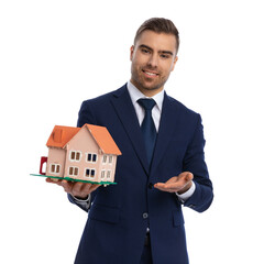 elegant young businessman in navy blue suit recommending house model