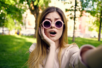 Cheerful woman in sunglasses outdoors in the park Green grass fresh air