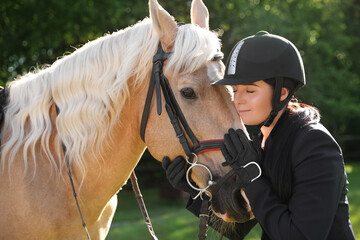 Fototapeta premium Young woman in horse riding suit and her beautiful pet outdoors on sunny day