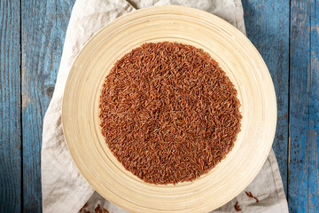 Red rice in a large wooden plate on a blue wooden table. Rustic style