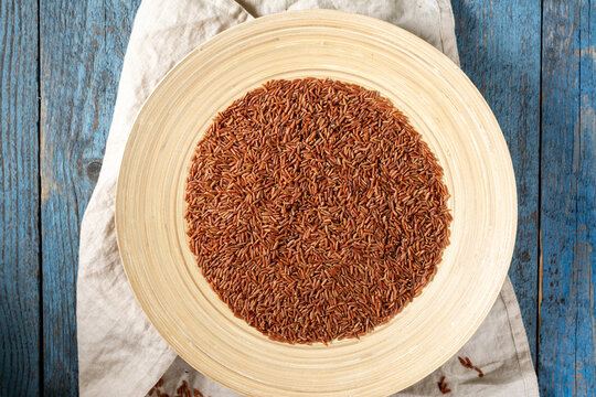 Red rice in a large wooden plate on a blue wooden table. Rustic style