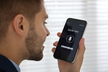 Young man using voice search on smartphone indoors, closeup