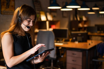 Beautiful caucasian woman in a headset is holding a digital tablet. Portrait of a business woman in the office