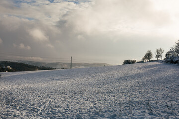 Fototapeta premium Winter snowy field with hills in the background, power lines, sunshine landscape