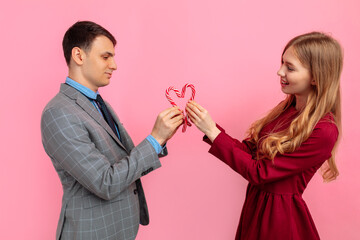 man and woman, make a heart of Christmas striped candies on a pink background, celebrate Valentine's Day