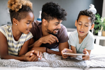 Happy father and children having fun with tablet, smiling at funny video, playing game