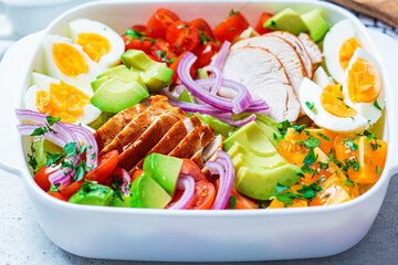 American cobb salad with chicken, avocado, egg, tomatoes and onions in white dish, light...