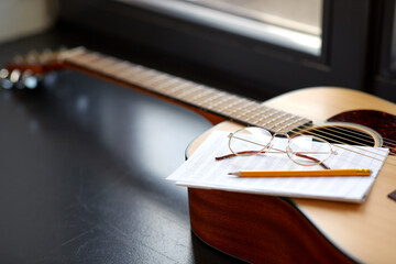 composing and music writing concept - close up of acoustic guitar with music book, pencil and...