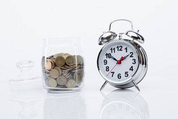 Bank with coins and alarm clock on a glass table. Time is money concept.