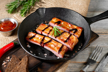 Boiled smoked pork ribs in a black cast-iron skillet on a gray wooden table. Fried pork ribs
