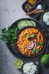 Vegan chickpea curry with rice and cilantro in black plate, dark background. Indian cuisine concept.