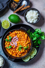 Vegan chickpea curry with rice and cilantro in black plate, dark background. Indian cuisine concept.