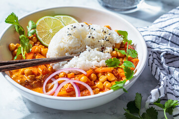 Vegan chickpea curry with rice and cilantro in white bowl, white marble background. Indian cuisine concept.