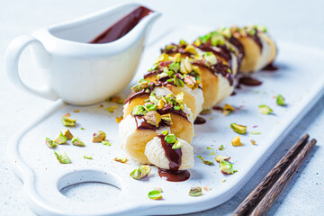 Sweet banana sushi with chocolate and nuts, white background. Vegan dessert concept.