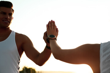 Fototapeta na wymiar Couple with fitness trackers giving each other high fives after training outdoors, closeup