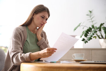 Worried woman reading letter at wooden table in room