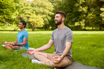 fitness, yoga and healthy lifestyle concept - men meditating in lotus pose at summer park