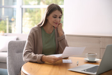 Woman reading letter at wooden table in room