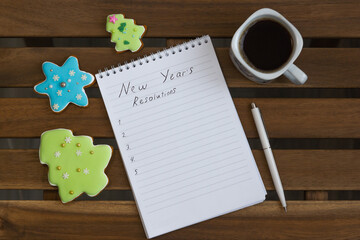 A notebook with plans for the new year, around the notebook are cookies in the form of Christmas trees and a cup of coffee