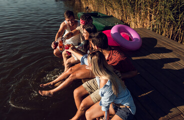 Group of friends sitting on the edge of a pier having fun and enjoying a summer day at the lake.