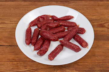 Small thin dry cured sausages on dish on a rustic table