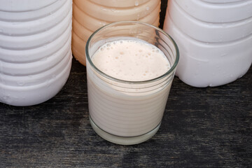 Glass of fermented milk drink against the plastic bottles