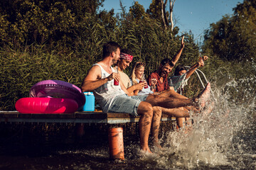 Group of friends sitting on the edge of a pier having fun and enjoying a summer day at the lake.