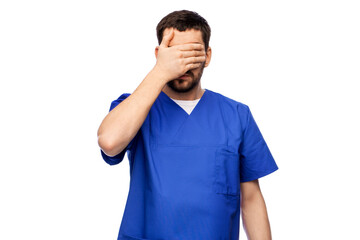 healthcare, profession and medicine concept - stressed doctor or male nurse in blue uniform covering his eyes with hand over white background