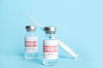 Vials with coronavirus vaccine and syringe on light blue background