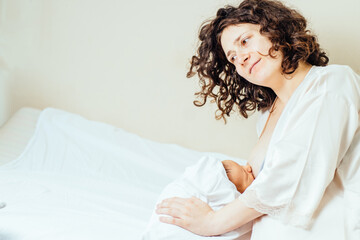 Young mother holding her newborn child. Mom nursing baby. Woman and new born boy in maternity hospital room. Mom lying on bed breast feeding.