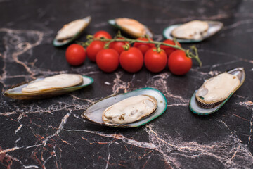 Fototapeta na wymiar Delicious and appetizing mussels and cherry tomatoes on a marble table