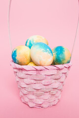 Multi-colored Easter eggs in a basket on a pink isolated background. Easter is a bright holiday.