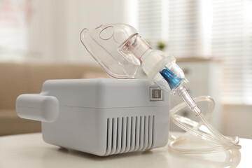 Modern nebulizer with face mask on white table indoors. Inhalation equipment