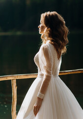 Luxury bride in a luxurious wedding dress enjoys the views of a mountain lake