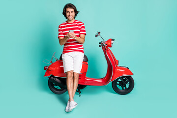 Fototapeta na wymiar Full length body size view of handsome cheery guy sitting on moped using device isolated over bright green turquoise color background