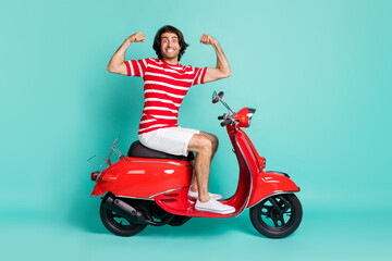 Fototapeta na wymiar Portrait of handsome cheerful strong guy sitting on moped showing muscles isolated over bright green turquoise color background