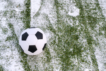 Soccer ball placed on snowy synthetic grass in winter on sports ground, copy space