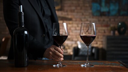 Elegant man tasting and serving red wine in a couple of wine glasses at home in a cosy dark room.