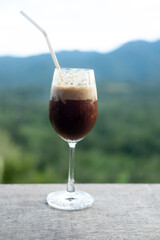 Two-layer irish coffee in a cocktail glass on wood table with mountain and forest background