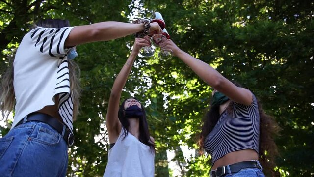 Three happy women friends toasting together with red wine - Millennials wearing face mask for protection infection from Coronavirus, Covid-19 - People having fun in the garden house at party