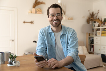 Easy communication. Happy young man posing for portrait at home looking at camera distracted from...