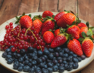 red berries, strawberries blueberries and currants on a plate on wooden table, healthy