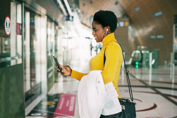 An attractive African woman is waiting for the subway and listening to music with headphones. Public transport, travel