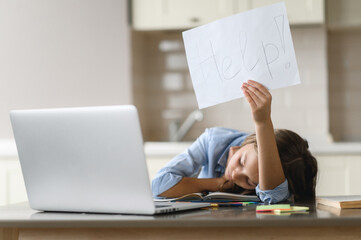 Distance learning. The schoolgirl is tired of studying. A frustrated caucasian schoolgirl, tired of studying at home, lies at her desk and holds a leaflet with the inscription help