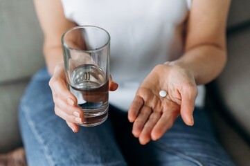 Top view of female hands with pill and water. Pain-relieving pill or enzyme in one hand of a woman and a glass of clean water in the other - obrazy, fototapety, plakaty