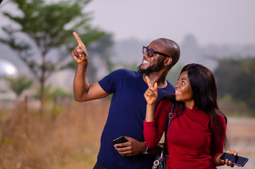 young african man and woman standing outside and delighted while using their smart phone