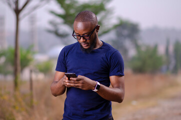 young african man standing outside and delighted while using his smart phone