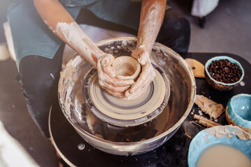 Close-up of the hands of a woman ceramist working with a potter's wheel in a cozy, bright workshop. A young experienced woman skillfully makes a mug, vase or plate. Creative people, pottery workshop