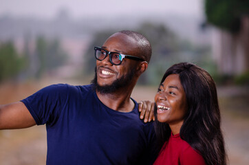 Naklejka premium young african man and woman standing outside and delighted while using a smart phone to take a picture