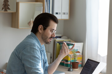 Concentrated young businessman speak to cell microphone working from home with paper electronic...